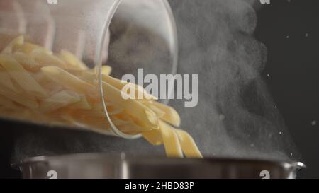 dry penne rigate poured in saucepan with boling water, wide photo Stock Photo