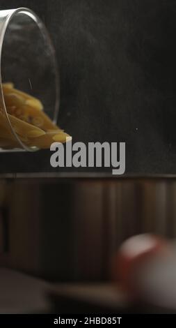 vertical shot dry penne rigate poured in saucepan with boling water, vertical photo Stock Photo