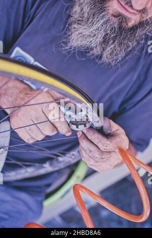 Bicycle mechanic with beard and dirty hands is tightening bicycle spokes with tool in aworkshop Stock Photo