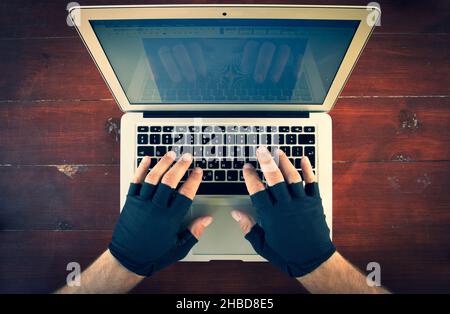 look down to the males hands with gloves typing on laptop keyboard on the red wood background. Background of working space. Stock Photo