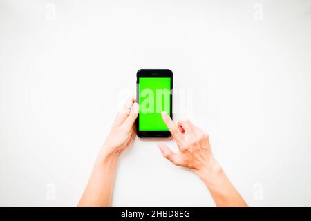 Females hand shows mobile smartphone with green screen in vertical position isolated on white background with finger tap screen. Mock up mobile techno Stock Photo