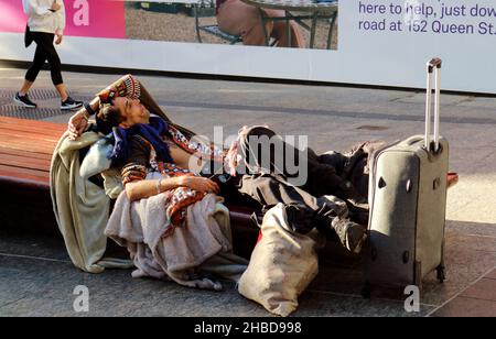 Traveller with bags and luggage resting comfortably on a city bench in Brisbane City Australia Stock Photo