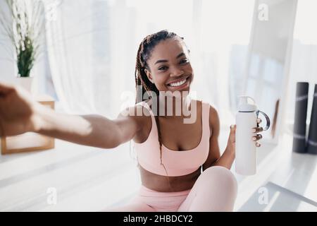 Smiling young African American lady with bottle of water taking selfie on break from home workout Stock Photo