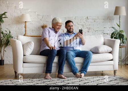 Happy young man using cellphone with older father. Stock Photo