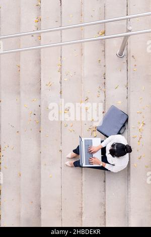 top view of an unrecognizable businesswoman working with her laptop computer sitting on a concrete staircase, concept of digital entrepreneur and urba Stock Photo