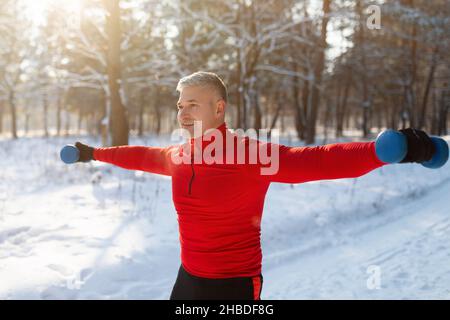 Outdoor strength workout. Determined senior man exercising with dumbbells, pumping up muscles at snowy forest Stock Photo