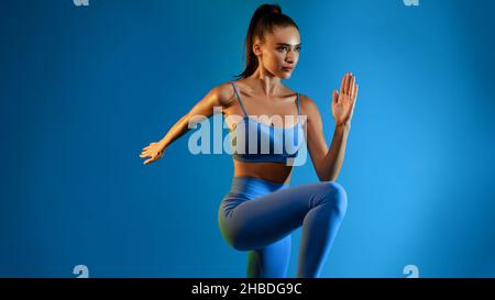 Fitness Woman Doing Elbow-To-Knee Crunch Exercising Standing Over Blue Background Stock Photo