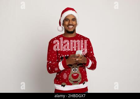 Cheerful black guy in Santa hat using smartphone Stock Photo
