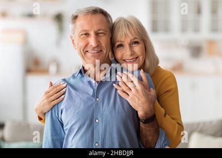 Senior Wife Embracing Husband Posing Together Standing In Kitchen Stock Photo