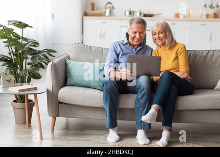 Cheerful Senior Spouses Using Laptop Watching Movie Onilne At Home Stock Photo