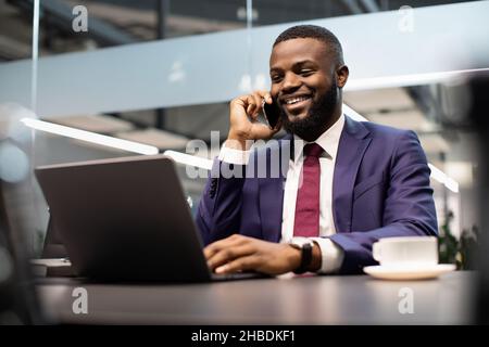 Smiling black manager working on laptop and talking on phone Stock Photo
