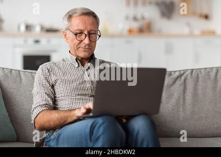 Senior Male Using Laptop Sitting On Couch At Home Stock Photo