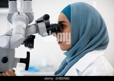 Modern Dentistry. Muslim Female Doctor In Hijab Using Dental Surgical Microscope, Closeup Stock Photo