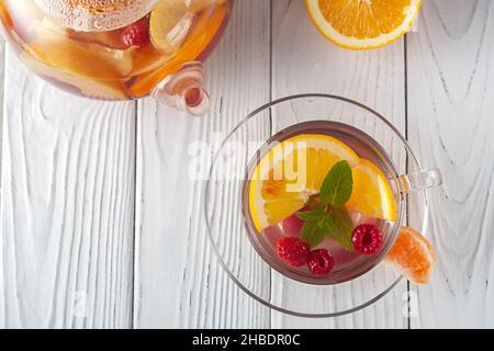 Fruit tea with berries, oranges and mint in a glass cup on a white wooden background Stock Photo