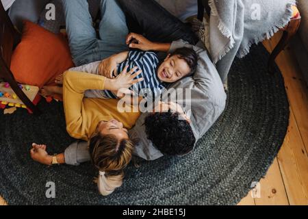 Overhead view of a little boy having fun with his mom and dad in their play area. Young boy laughing cheerfully while lying on top of his parents. Fam