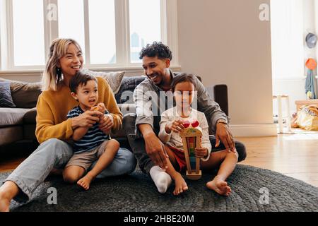 Two young parents playing with their son and daughter in the living room. Mom and dad having fun with their kids during playtime. Family of four spend
