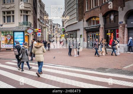 Amsterdam, Netherlands. 19 dec 2021. People in small groups strolling through the Kalverstraat, one of the most busy shopping streets of Amsterdam, on the first day of the full lock down. As from Sunday 19th of Dec. a full lock-down is announced by the government of the Netherlands. Only essential shops can stay open and outdoors group gatherings of max 2 people over 13ys of age are allowed unless they belong to the same household. Credit: Steppeland/Alamy Live News Stock Photo