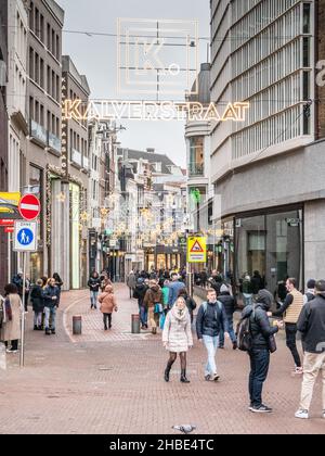 Amsterdam, Netherlands. 19 dec 2021. People in small groups strolling through the Kalverstraat, one of the most busy shopping streets of Amsterdam, on the first day of the full lock down. As from Sunday 19th of Dec. a full lock-down is announced by the government of the Netherlands. Only essential shops can stay open and outdoors group gatherings of max 2 people over 13ys of age are allowed unless they belong to the same household. Credit: Steppeland/Alamy Live News Stock Photo