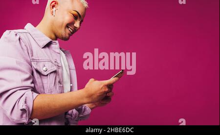 Non-conforming young man playing his favourite music. Happy young man using a smartphone while wearing wireless earphones in a studio. Queer man smili Stock Photo