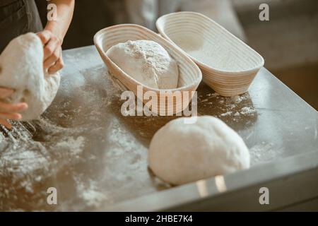 Worker with raw dough loaf prepares bread at metal table in bakery Stock Photo
