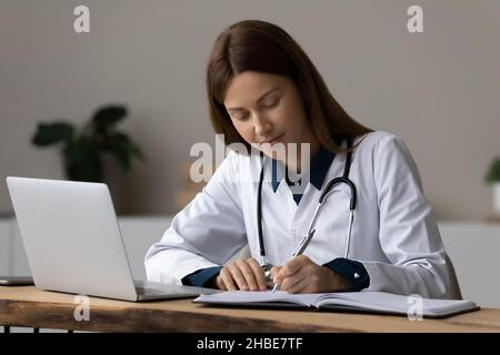 Concentrated young woman medical worker take notes at workplace Stock Photo