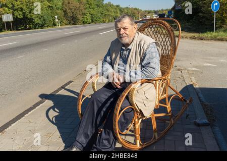 Caucasian senior man resting while sitting in a wicker rocking-chair at roadside at sunny autumnal day Stock Photo