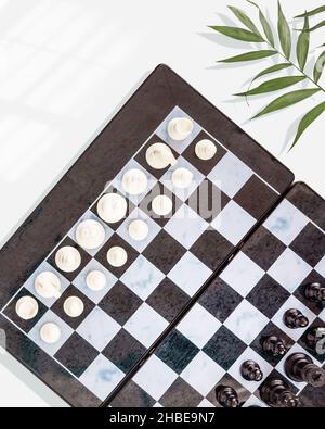 Chess game. Chess composition with a chess board with placed pieces and palm leaves on a blue background. Chess competition. Flat lay Stock Photo