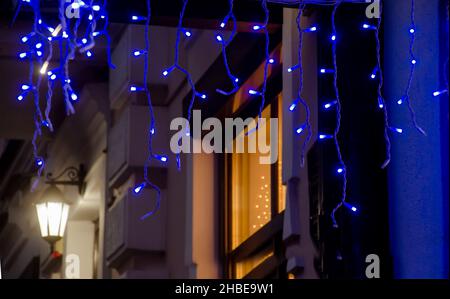 Christmas decoration in the city. A luminous garland of dark blue color on the window on the street. Glowing illumination on the street. Street lamp on the building. Stock Photo
