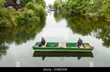 Two Men Fishing On A Chain Moored Punt Boat In The Bridge Pool  On The River Avon Christchurch, UK Stock Photo