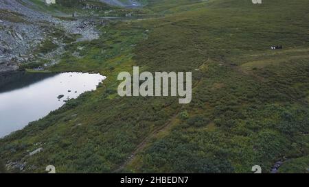 Aerial view of people ride horses on the mountain field. Horseback riding in the mountains , swimming in the lake. Horses walk on a green grass. Aeria Stock Photo