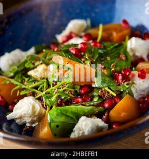 Delicious persimmon salad with pomegranate and arugula on the table, serving in a restaurant, menu food concept. Stock Photo