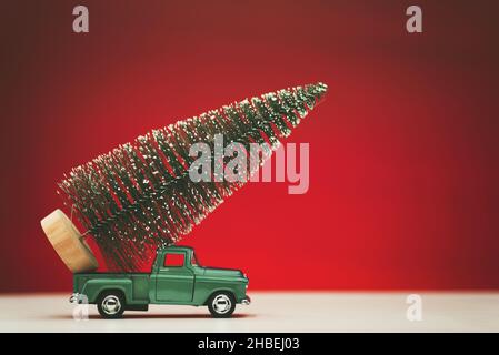 Green colored toy model pick up truck carrying a pine tree on a matte red background. Stock Photo
