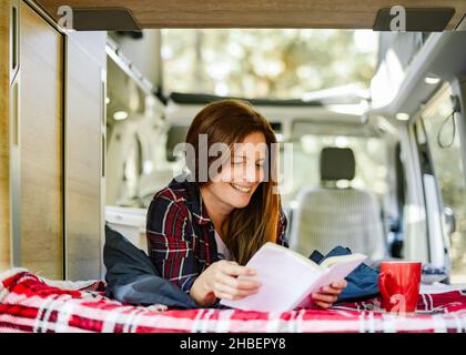 Smiling woman reading book in traveling van Stock Photo