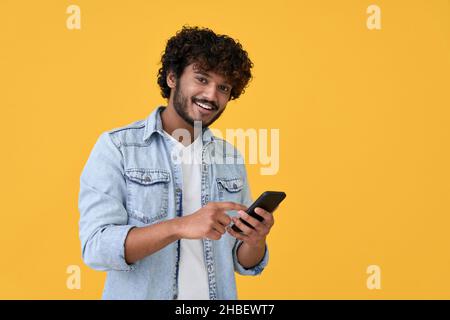 Smiling indian young man using cell phone isolated on yellow background. Stock Photo