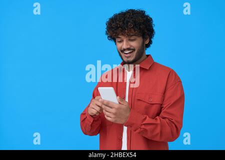 Happy indian young man using mobile phone isolated on blue background. Stock Photo