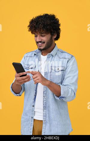 Happy indian young man using cell phone isolated on yellow background. Stock Photo