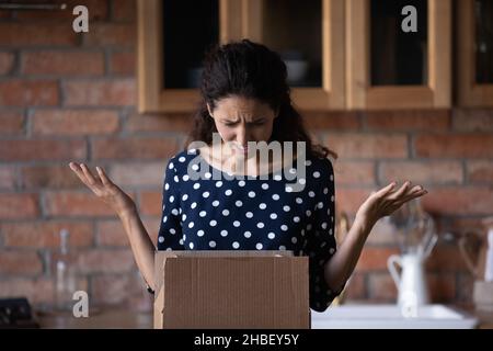 Unhappy anxious young latin woman unboxing carton parcel. Stock Photo