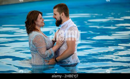 Stryi, Ukraine August 12, 2021: a pregnant woman and her husband swim in the pool, pregnant woman in a dress in the pool. Stock Photo