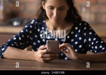 Smiling latin woman using smartphone, sitting at table. Stock Photo