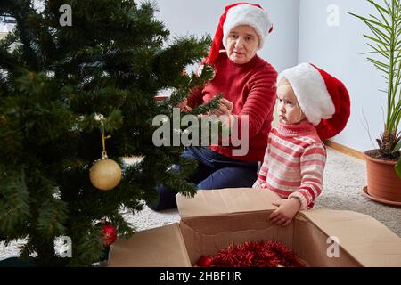 Merry Christmas and Happy Holidays. Grandmother and granddaughter decorate a Christmas tree at home. lifestyle. Stock Photo