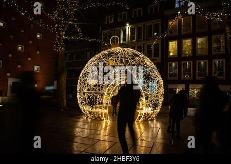 Nijmegen, Netherlands. 18th Dec, 2021. People are seen walking past a big lit Christmas ball.On the same day that Prime Minister Rutte announced a strict lockdown in the Netherlands, in order to prevent the rapid advance of the Omicron variant, for the second year in a row, eight impressive lit sculptures have been placed around the city center of Nijmegen to cheer the people up. The new measures will remain in effect until January 14th. Credit: SOPA Images Limited/Alamy Live News Stock Photo
