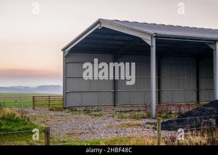 large empty corrugated barn with low clouyd background and sun set, Wiltshire UK Stock Photo