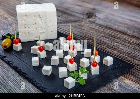 Feta Cheese Cubes on wooden cutting board. Square cubes of feta cheese isolated on wood board with knife. Stock Photo