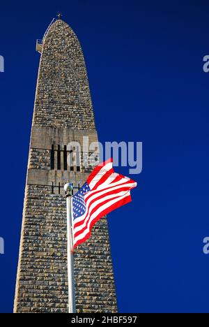 An American flag waves in front of the Bennington Battle Monument in Vermont.  The obelisk honors the Green Mountain Boys of the American Revolution Stock Photo