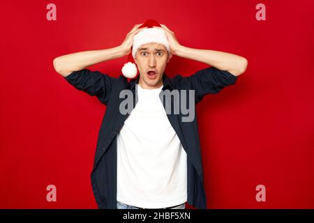 young shocked man amazed with wide open eyes, mouth holding head with arms. isolated red background Stock Photo
