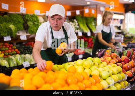 Seller in uniform holding fresh oranges Stock Photo