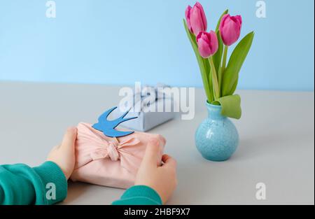 Eco gift decorated with a swallow made of wood in the hands of a child. Spring still life scene. space for text Stock Photo