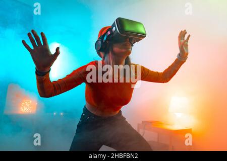 Wireless technologies. Young woman using virtual reality glasses in the dark room with neon lighting. Stock Photo
