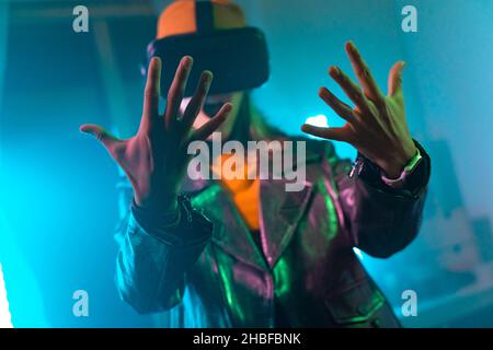 Wireless technologies. Young woman using virtual reality glasses in the dark room with neon lighting. Stock Photo