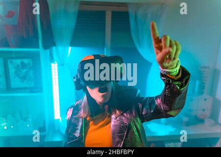 Wireless technologies. Young woman using virtual reality glasses in the dark room with neon lighting. Stock Photo